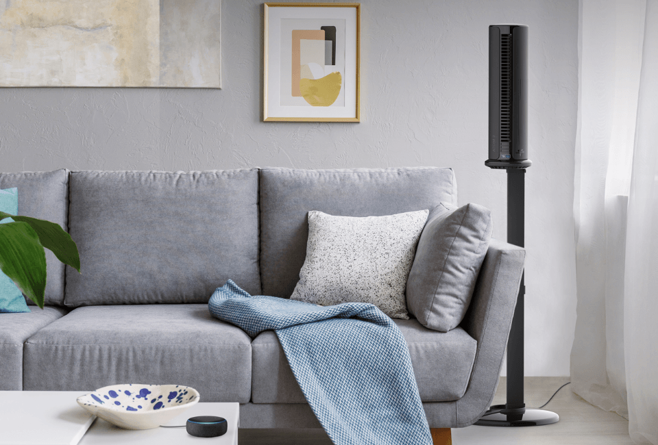 Atom 2S AE Compact Oscillating Tower Circulator with Stand in living room Atom 2S AE Compact Oscillating Tower Circulator with Stand in living room situated next to a gray sofa. An alexa device is on the table by the sofa