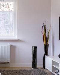Lifestyle of Vornado OSC54 32" Oscillating Tower Circulator in an apartment next to a window and a large vase with colorful leaves in it.