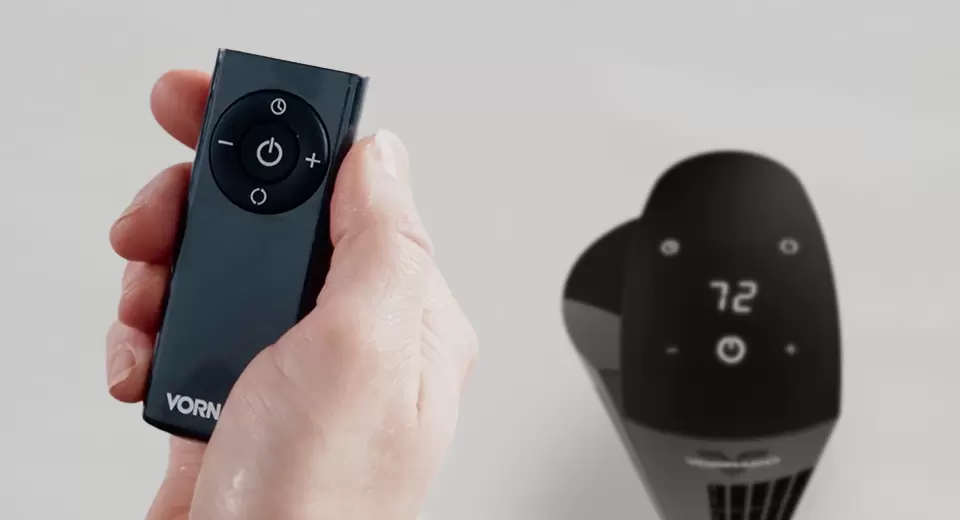 Closeup of a hand holding a OZI42DC Tower Circulator remote. blurred in the background is a OZI42DC Tower Circulator.