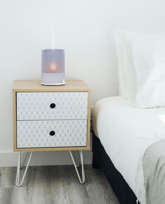 Lifestyle image of VOTIV 4 Ultrasonic Humidifier on a nightstand near a bed