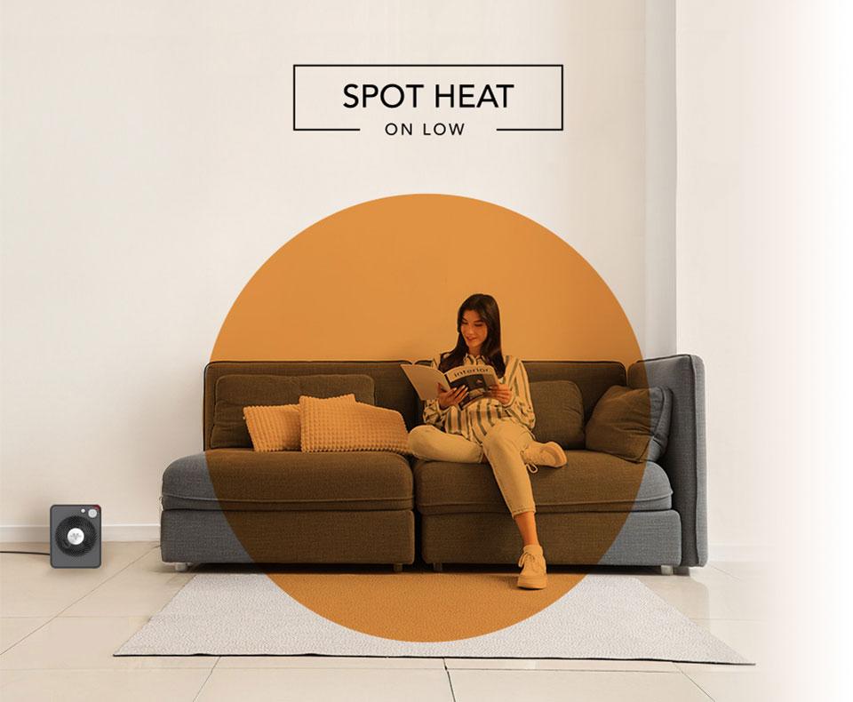 VMHi300 Spot Heat Woman reading on her couch with the VMHi300 heater on the floor. There is an orange circle overlay on her to indicate spot heat on low.