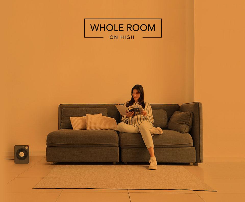 VMHi300 Whole Heat Woman reading on her couch with the VMHi300 heater on the floor. There is an orange overlay to indicate whole room heat for a small room on high.