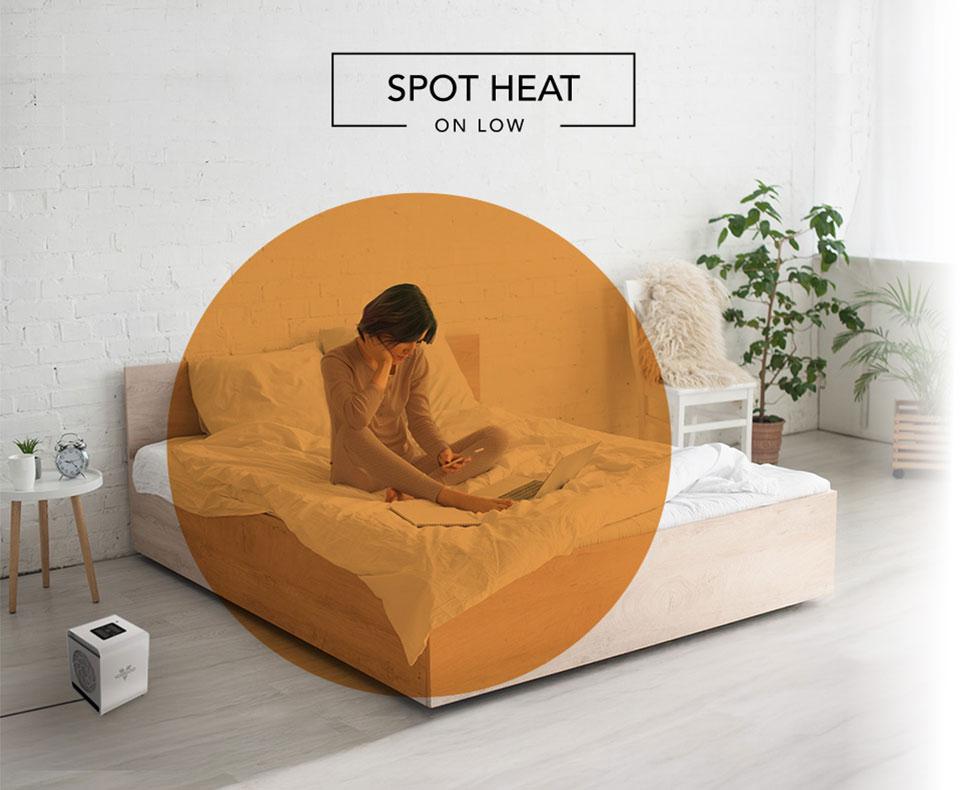 VMHi500 Spot Heat Woman reading on her bed with the VMHi500 heater on the floor. There is an orange circle overlay on her to indicate spot heat on low.