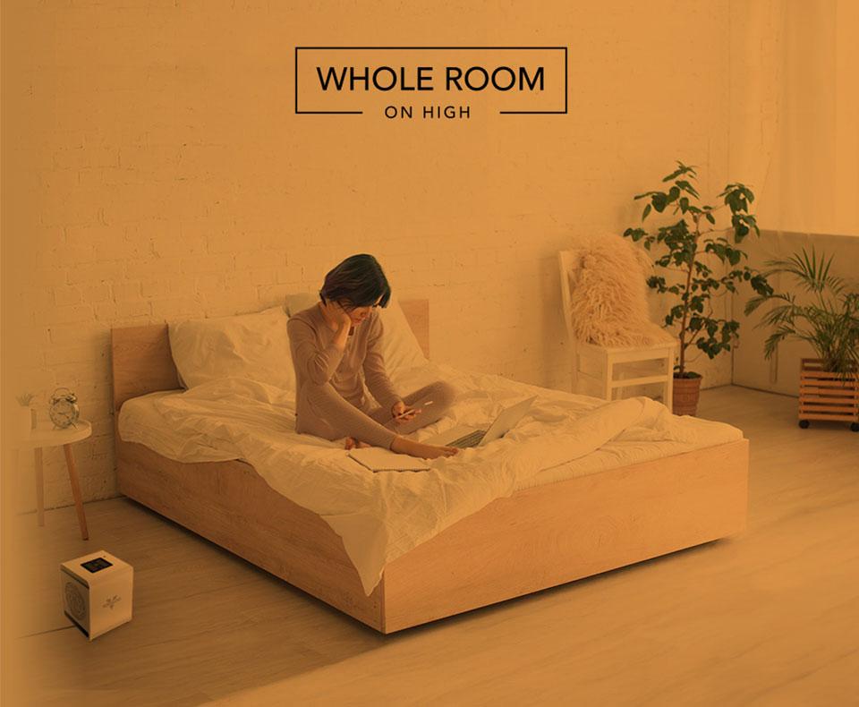 VMHi500 Whole Room Heat Woman reading on her bed with the VMHi500 heater on the floor. There is an orange overlay to indicate whole room heat for a small room on high.
