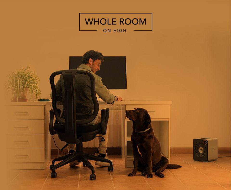 VMHi600 Whole Room Heat Man sitting at desk with smiling at his dog. A VMHi600 heater is on the floor nearby. There is an orange overlay to indicate whole room heat.