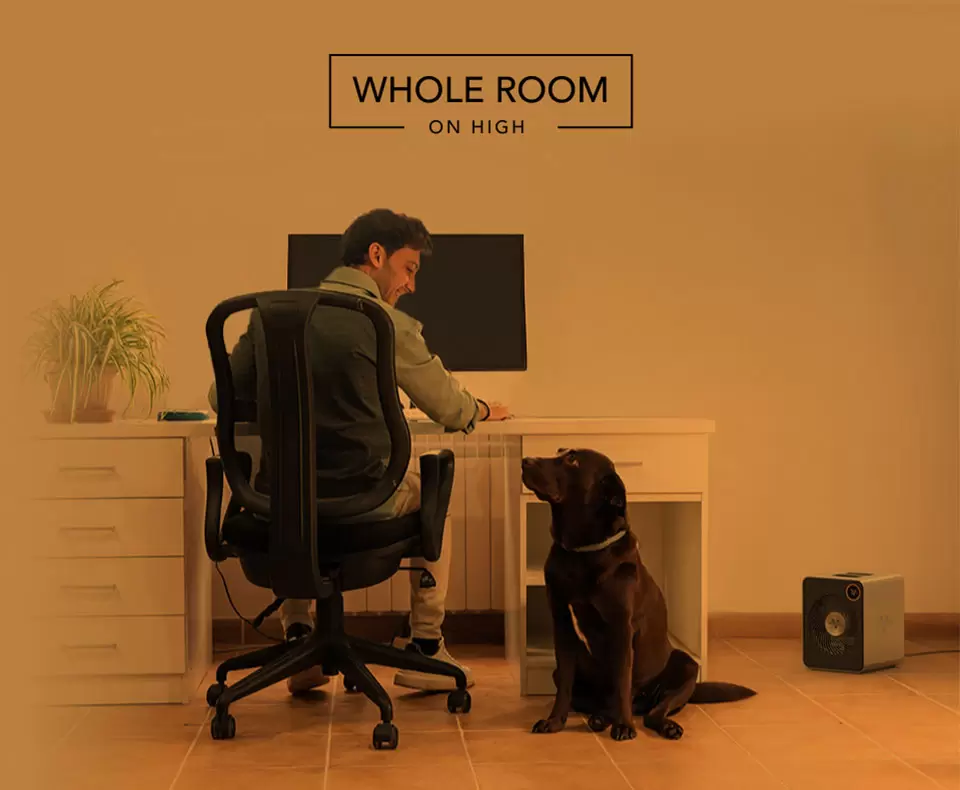 VMHi600 Whole Room Heat Man sitting at desk with smiling at his dog. A VMHi600 heater is on the floor nearby. There is an orange overlay to indicate whole room heat.