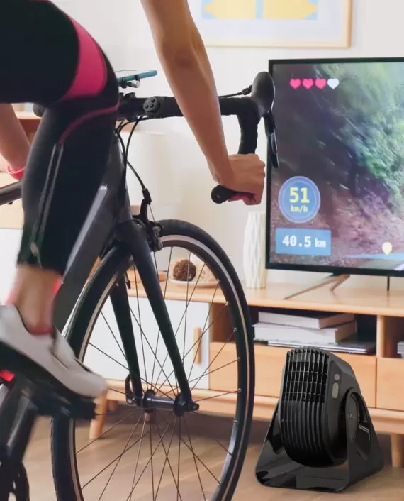 Woman in athletic clothing cycling in front of a Vornado FLY MAX and TV