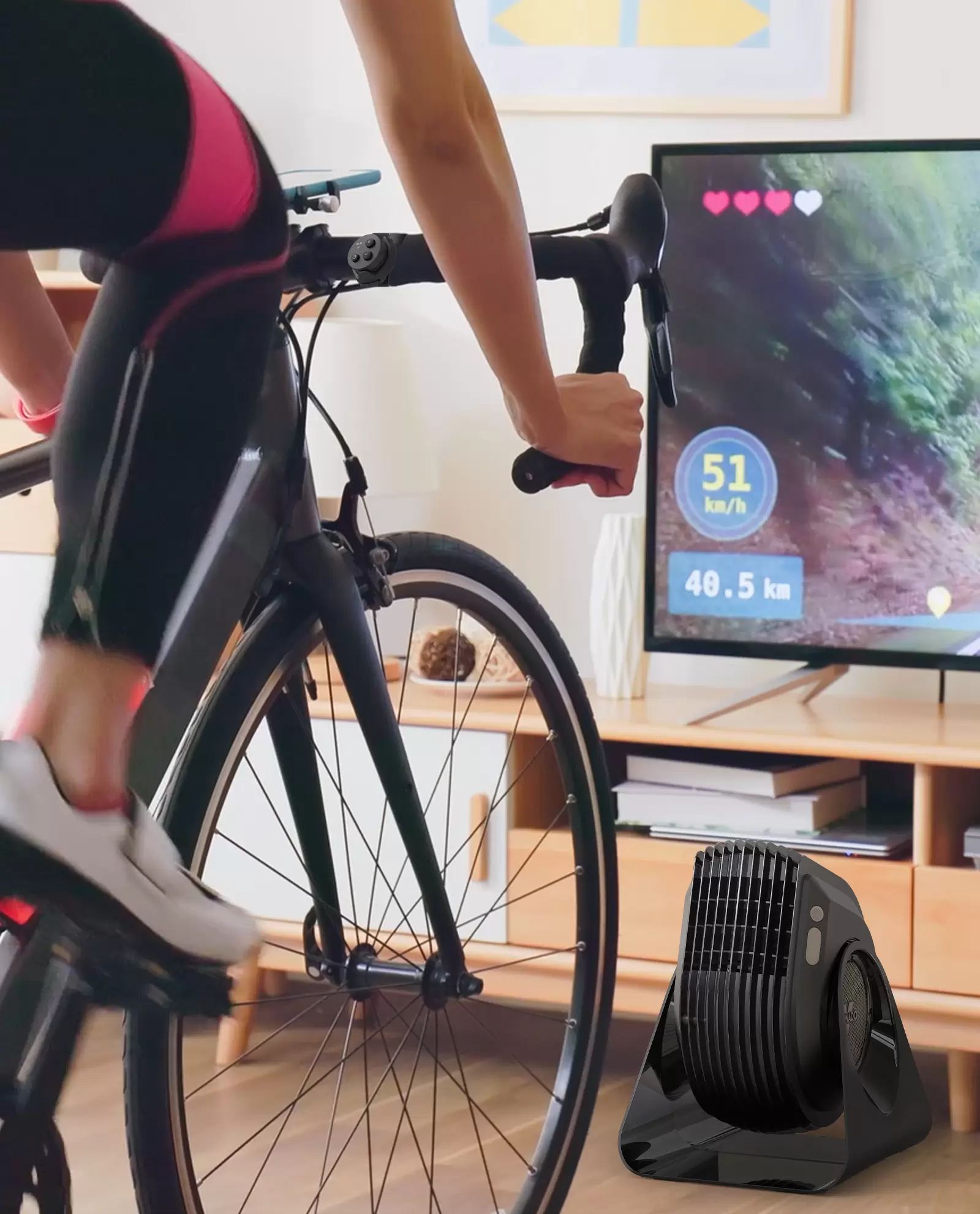 Woman in athletic clothing cycling in front of a Vornado FLY MAX and TV