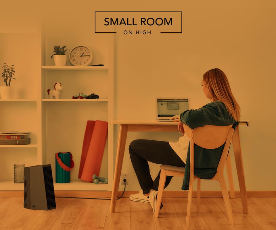 Woman sitting at desk with the Rise 12 H heater on the floor. There is an orange overlay to indicate whole room heat for a small room on high.