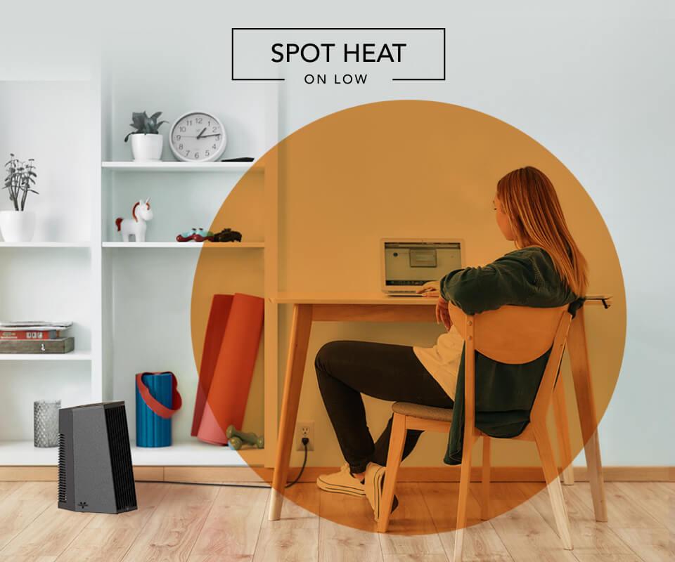 Woman sitting at desk with the Rise 12 H heater on the floor. There is an orange circle overlay on her to indicate spot heat on low.