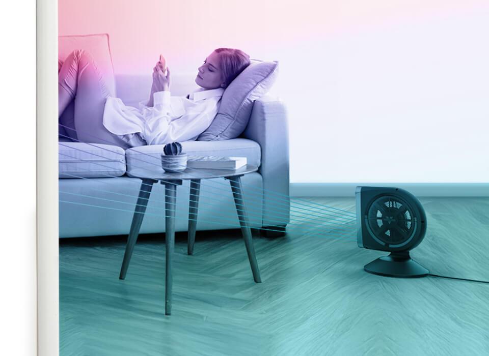 A woman relaxes on her couch as Strata 8T blows cool are on her. There is a light pink to blue overlay.