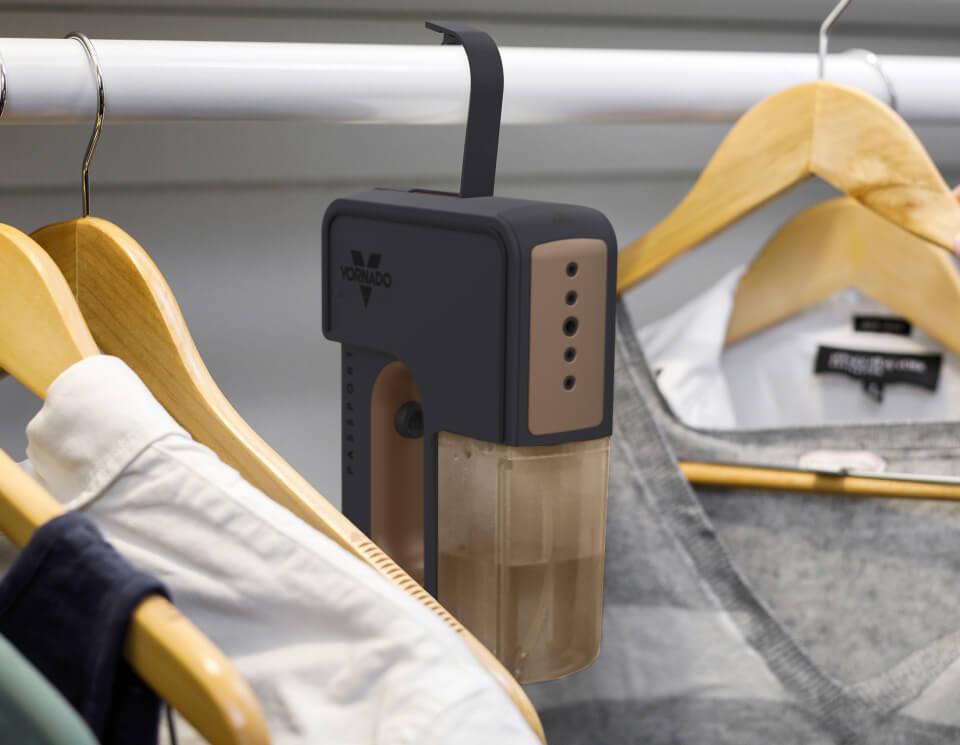 The passport handheld garment steamer hanging in a closet with its integrated hook next to clothes.