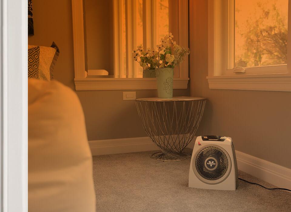 AVH10+ Whole Room Part of a bedroom seen through an open door with an orange gradient to show whole room heat circulation. AVH10+ is on the floor.