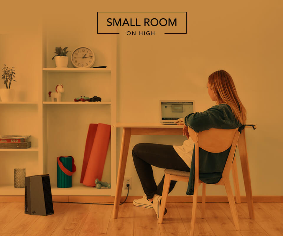 Woman sitting at desk with the Rise 12H heater on the floor. There is an orange overlay to indicate whole room heat for a small room on high.