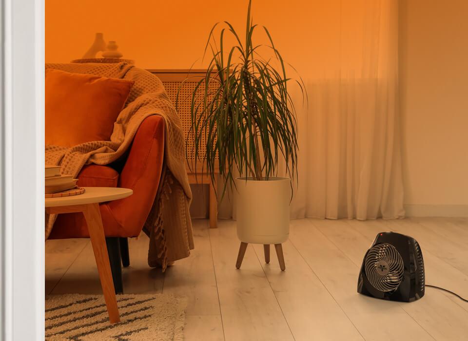 VH240 Whole Room Part of a living room seen through an open door with an orange gradient to show whole room heat circulation. VH240+ is on the floor near a couch.