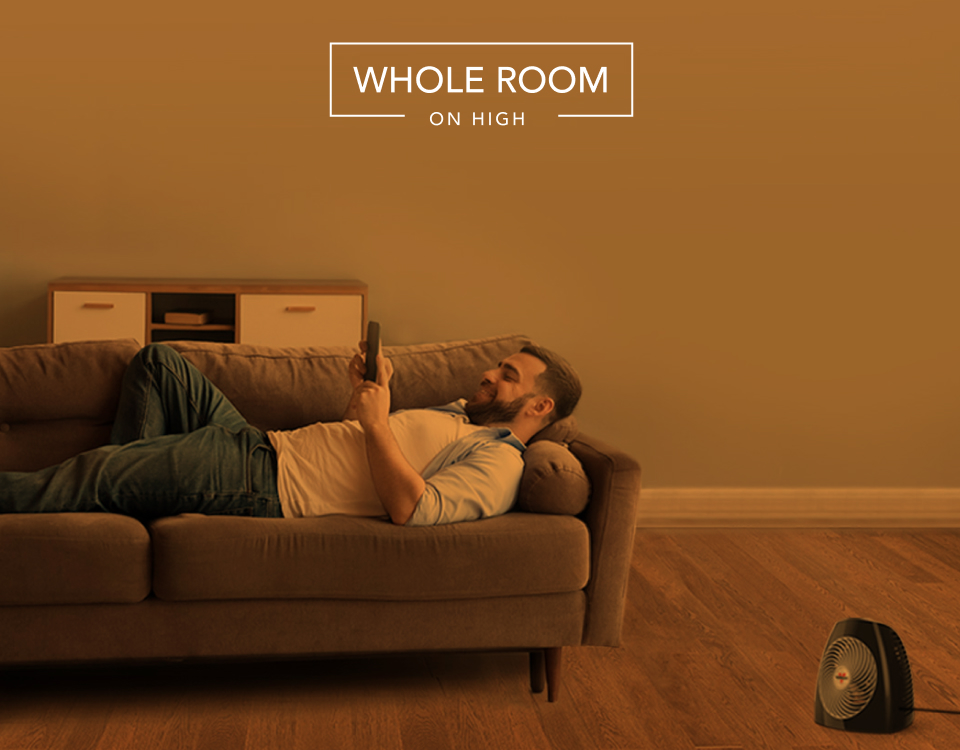 MVH Whole Room Man laying on couch with the MVH heater on the floor. There is an orange overlay to indicate whole room heat for a small room on high.