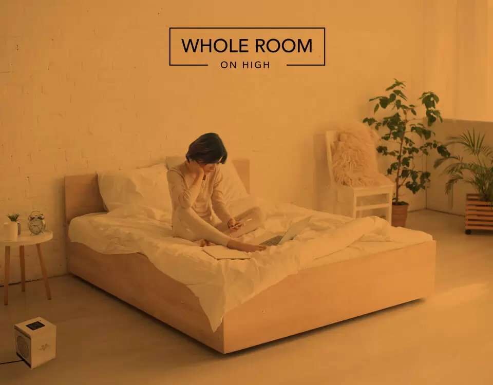 VMHi500 Whole Room Heat Woman reading on her bed with the VMHi500 heater on the floor. There is an orange overlay to indicate whole room heat for a small room on high.