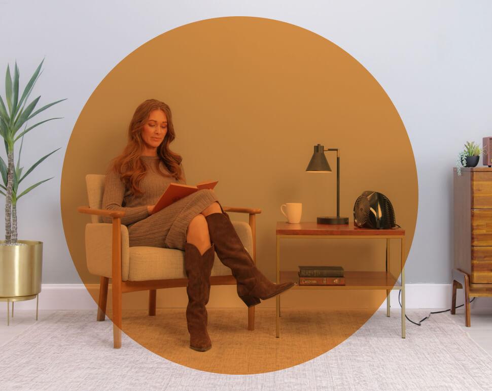 Woman reading in her chair with the VH204 heater on the side table. There is an orange circle overlay on her to indicate spot heat on low.